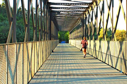 Runner crossing a metal bridge at sunrise during morning trainin