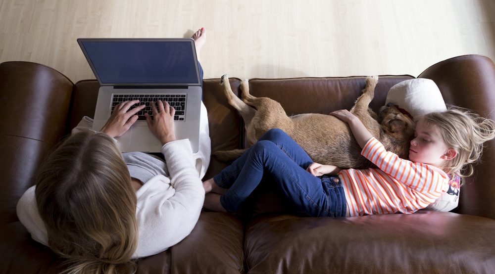 woman using laptop while daughter and dog sleep
