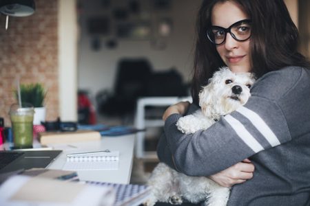Young woman playing with her dog while sitting at desk in front